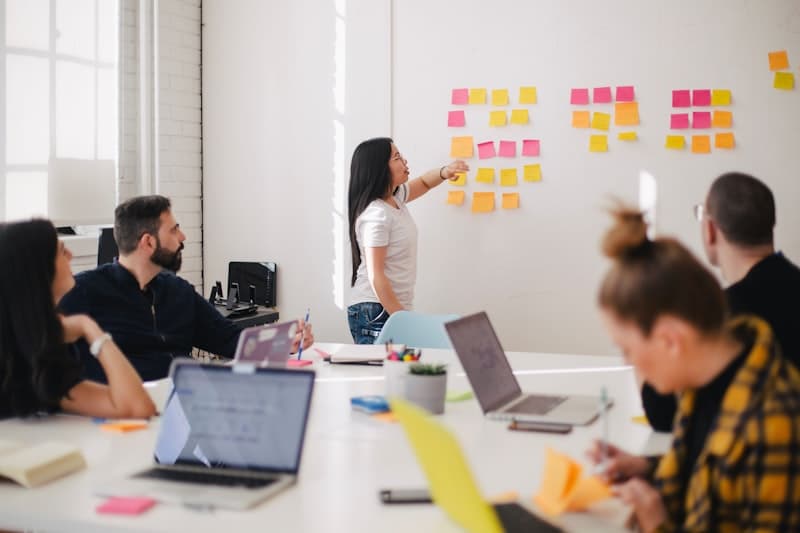 Une réunion où une personne organise des post-it au mur pendant que d'autres travaillent sur leurs ordinateurs
